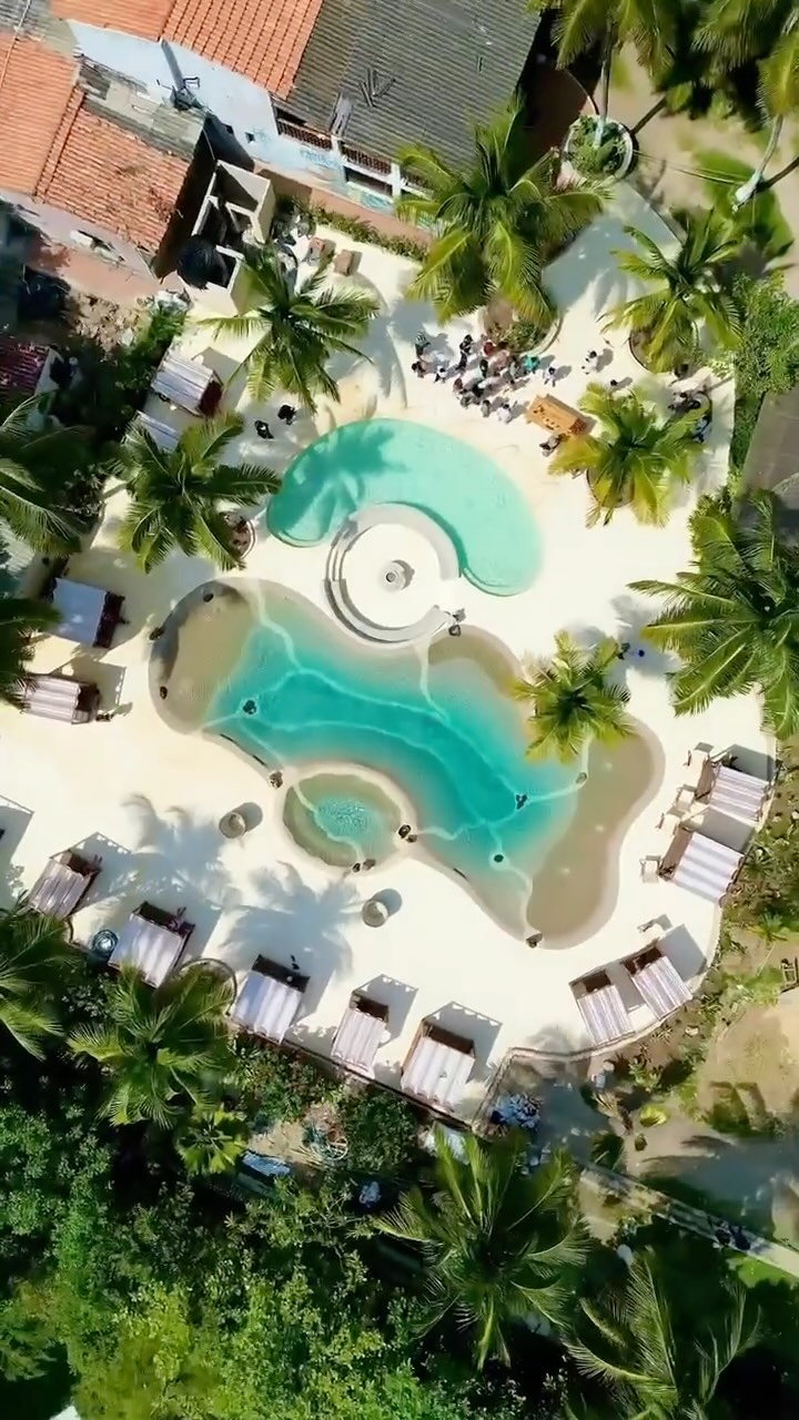Beach club with curved pools and palm trees, seen from above
