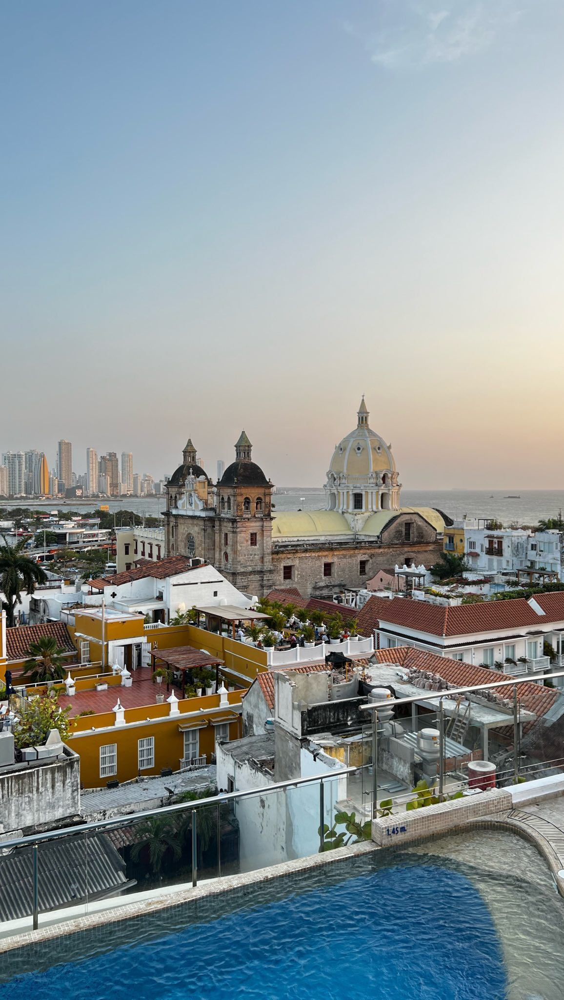Sunset over the walled city of Cartagena from a rooftop pool, with the dome of San Pedro Claver and the sea behind