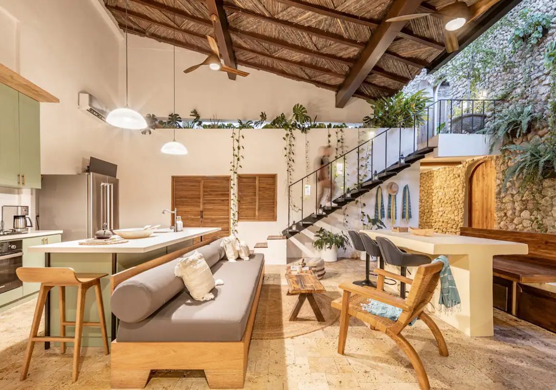 Open living room of a Cartagena house with a stone wall, plants and a cane roof