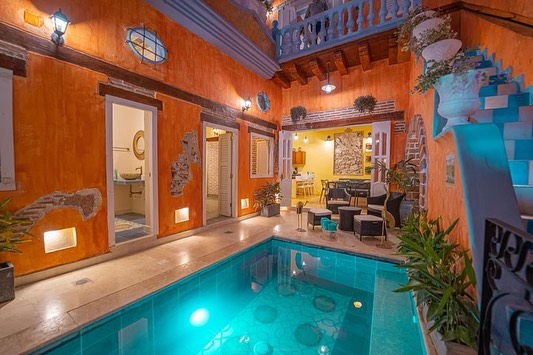 Courtyard pool of a colonial house in Cartagena, orange walls and a lit dining room