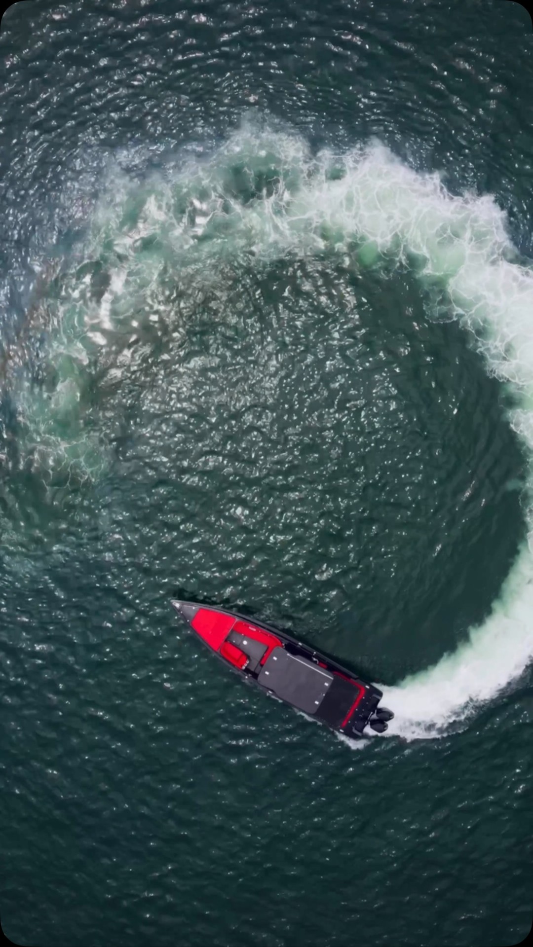 A black and red speedboat carving a circle of white wake on the Caribbean, seen from above